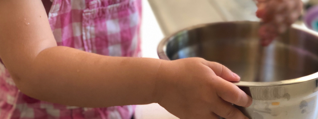 Hands of a little girl holding a bowl while cooking