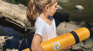 girl holding a yellow yoga mat for kid while walking outside. Practising yoga anywhere is one of the best benefit of practising mindfulness in nature. With this rainbow gum yoga mat that is easy to carry with its straps attached to it.